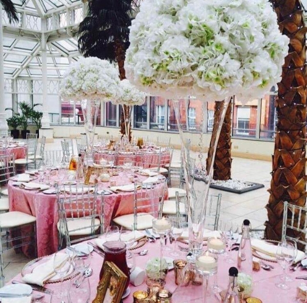 Round tables with pink tablecloths dressed for a wedding with tall table decorations of white flowers