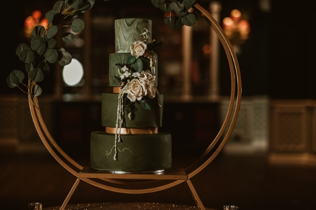 green and gold iced wedding cake framed by a hoop backdrop