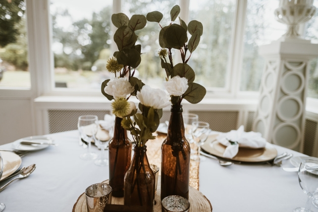 wedding centre pieces of brown glass bottles filled with white flowers and foliage