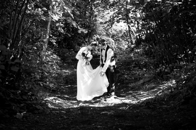 groom holding brides skirt. They are in the woods