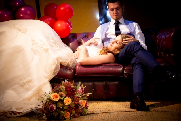 bride and groom on sofa. Bride is lying with head in groom's lap