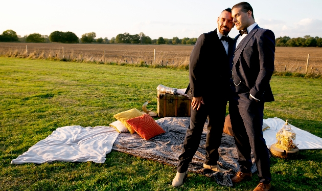 Two grooms standing in wedding field as the sun sets