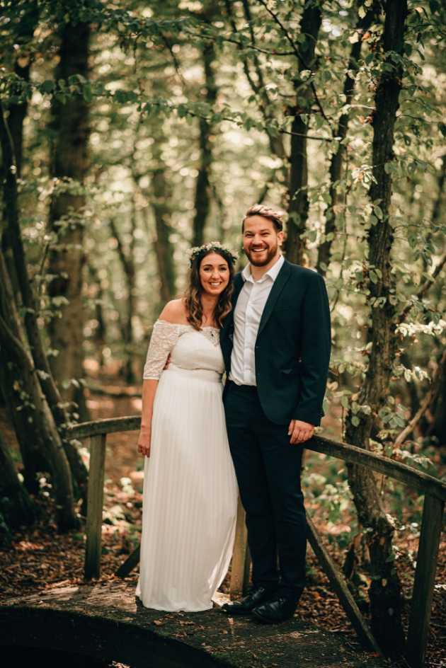 Bride and groom standing on small woodland bridge