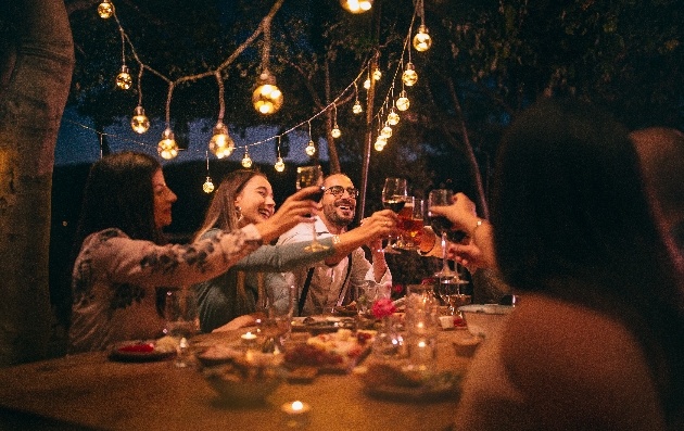 Group of friends celebrating over dinner and wine underneath festoon lighting