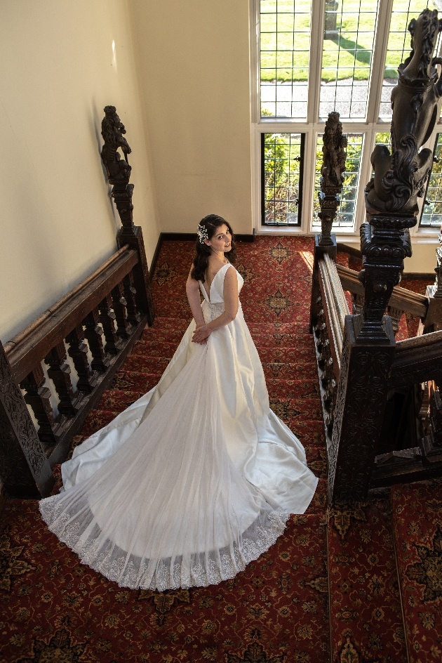 Bride at the top of the stairs at Broome Park looking back over her shoulder