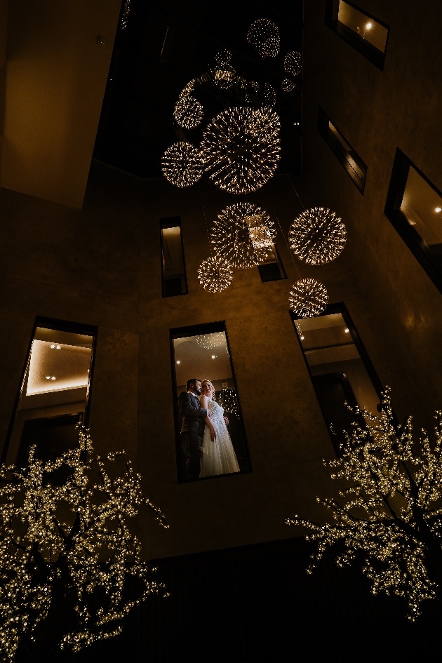 Bride and groom viewed through an upper window at One Warwick Park with venue's twinkly light installation in the foreground