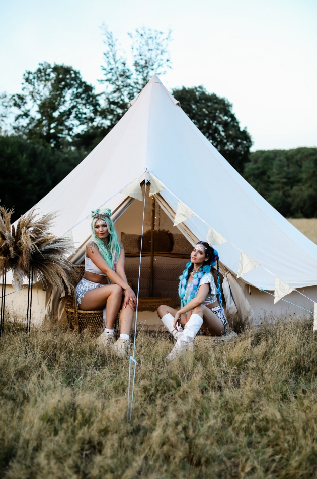 two models one with acqua hair one with blue sit outside bell tent