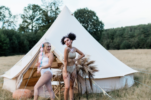 two women pose outside bell tent with pampas grass arrangement