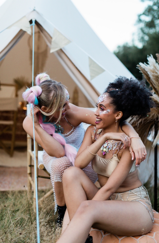two hens share a joke with bell tent in background decorated in beige bunting