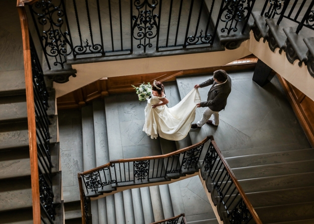 bride walking down stair in her wedding dress train being held by a man