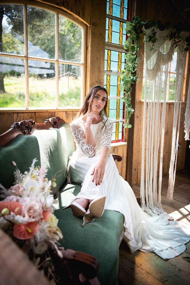 beautiful bridal portrait sitting on green velvet chaise longe bouquet in foreground with macrame backdrop