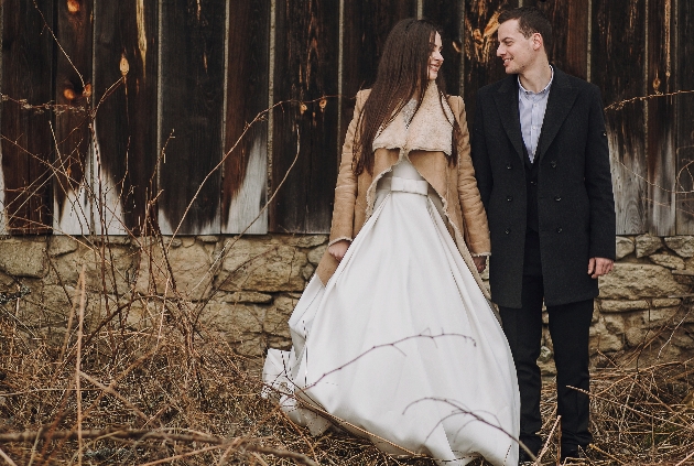 bride and groom outside in front of barn door bride in wedding dress with fur coat 