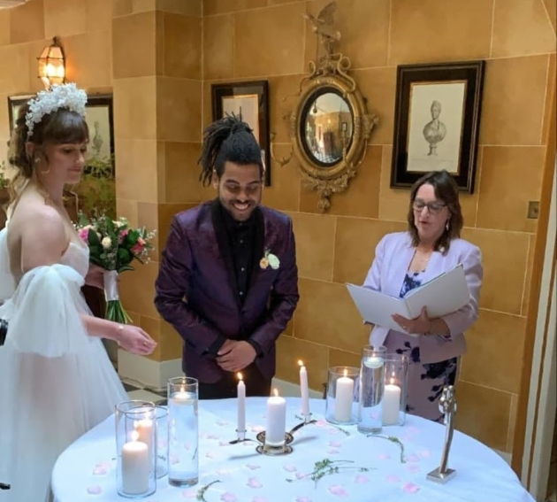 couple standing in front of a table lighting candles with a celebrant speaking from a book