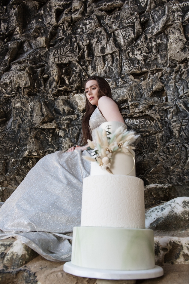 model sitting on rocks at beach in Kent green and white cake in the foreground