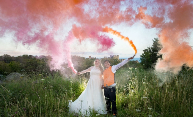 Couple with pink and orange smoke bombs and Fort Burgoyne in the background