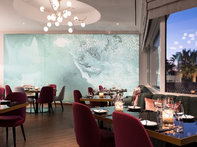 restaurant with red velvet chairs and black table with a large marble effect wall mural and feature light pendant 