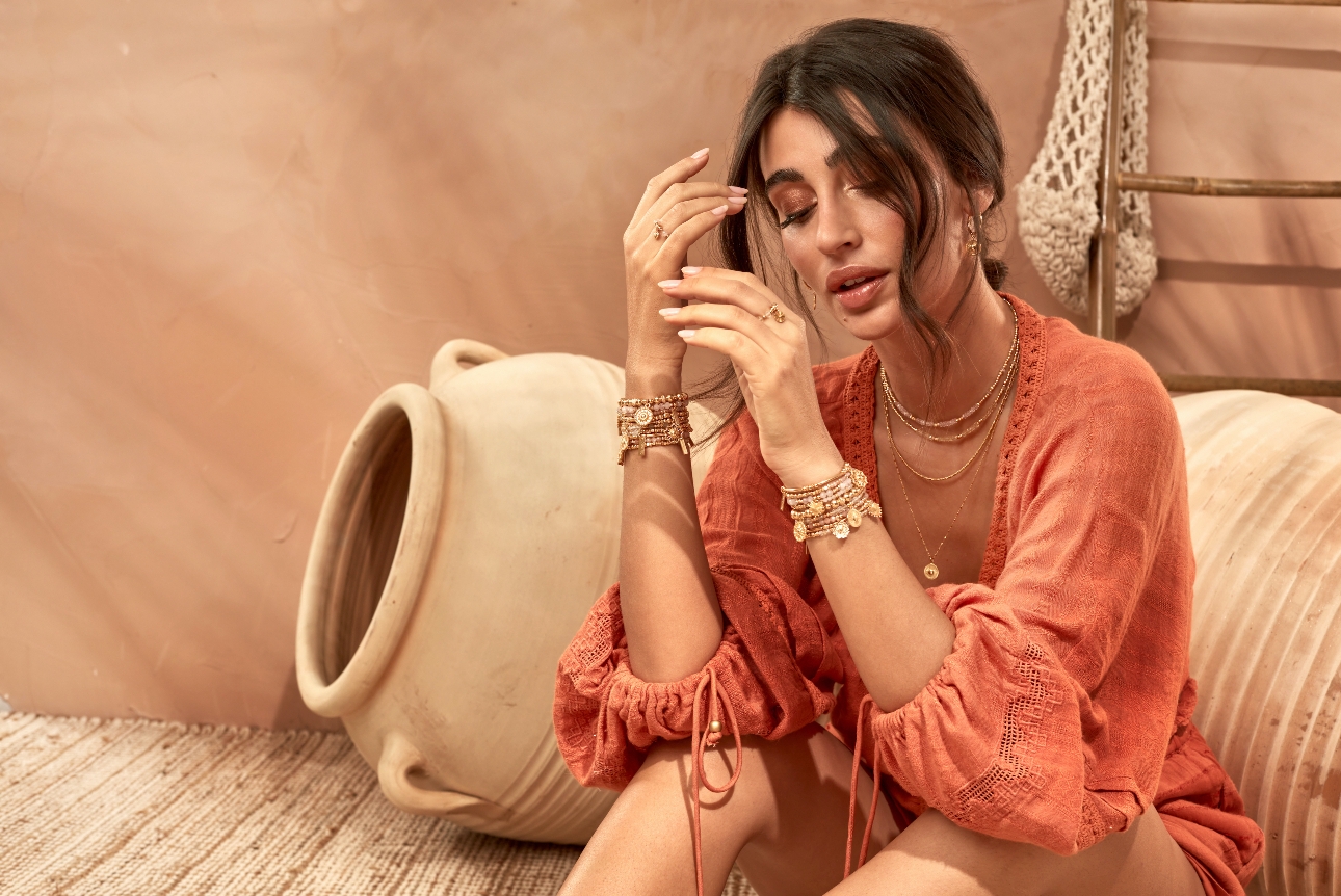 model in peach linen top wearing lots of layered gold bracelets and rings
