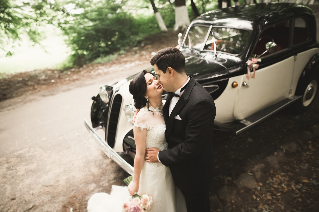 bride and groom standing in front of a black and white wedding car