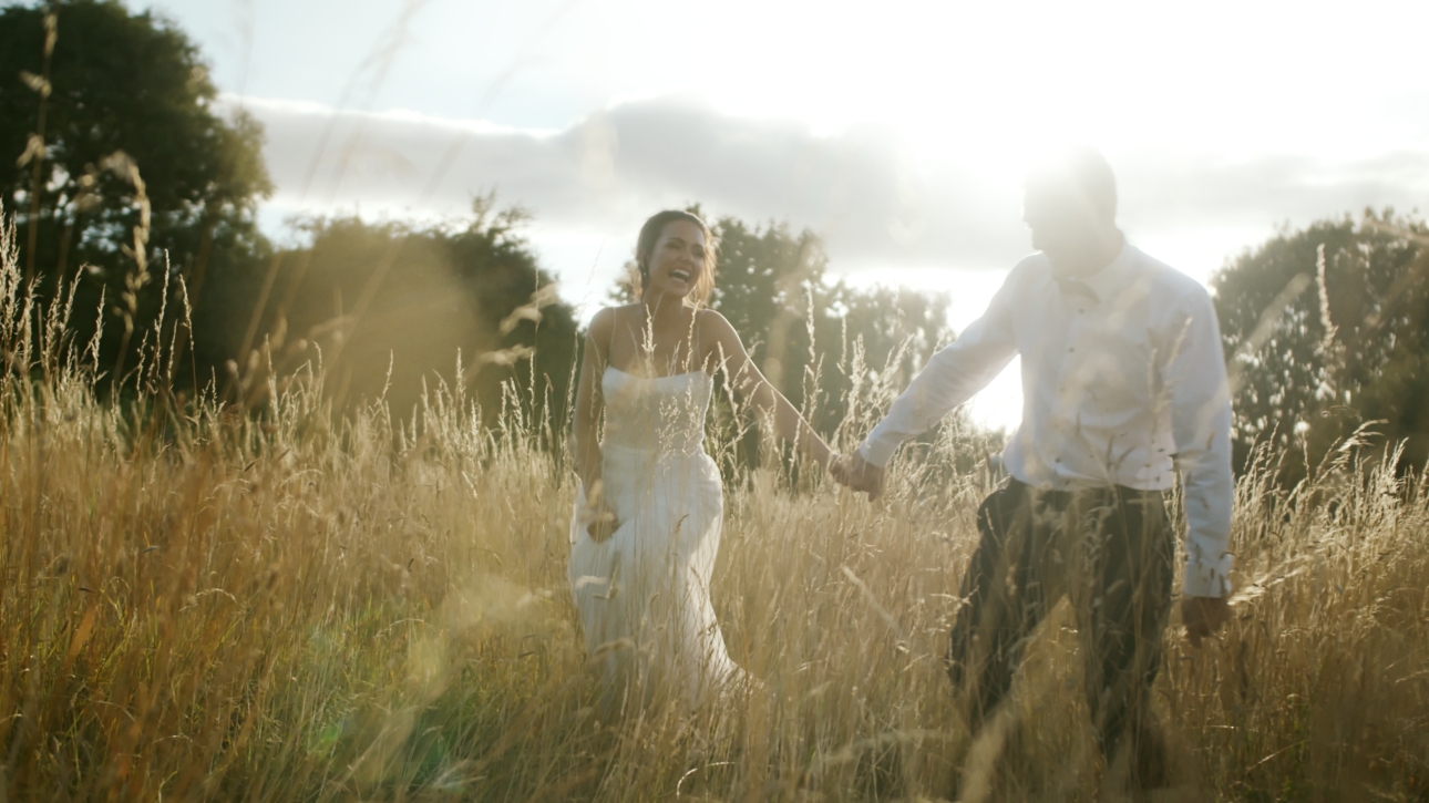 couple holding hand in wedding attire walking through a field and dusk