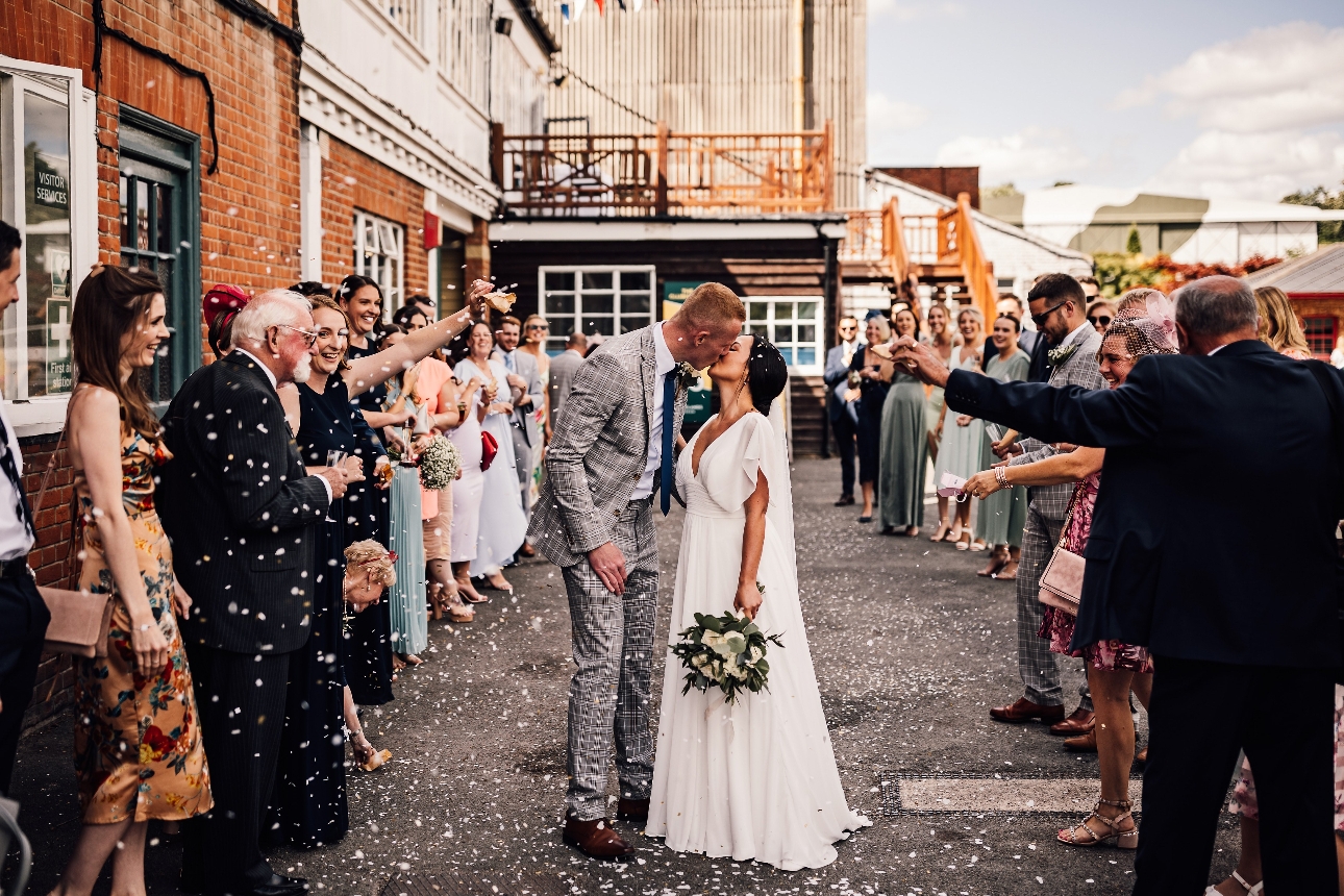 bride and groom kissing having confetti thrown on them outside of museum