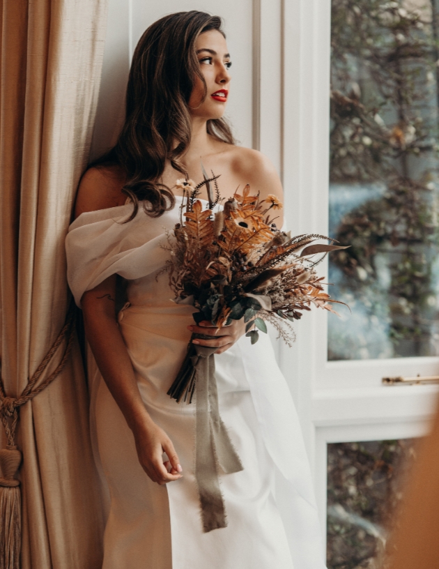 Hollywood glam bride gazing out of window holding dried flower bouquet