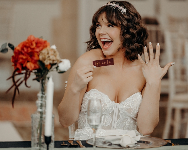 bride laughs as she holds up her bride place name and shows off her wedding ring