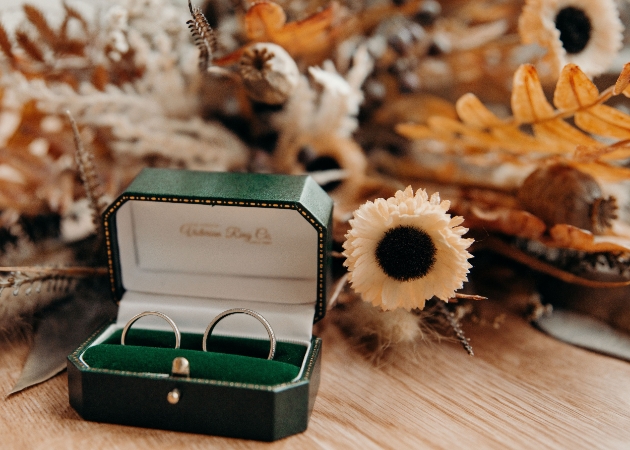 wedding rings in a green box with flowers in the background