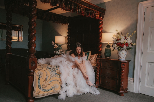 bride putting on her shoes sitting on four-poster bed in Stone Court House