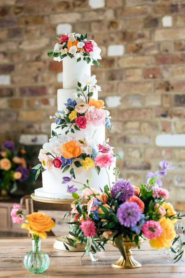 Beautiful white wedding cake covered in colourful sugar flowers in bring shades