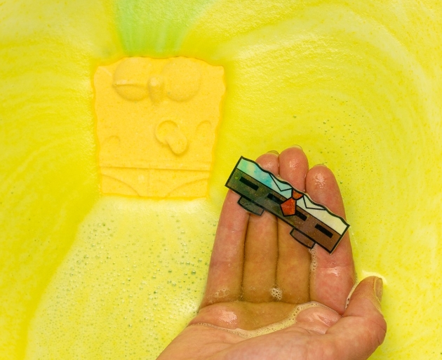 Yellow bath bomb in water with cartoon shorts on hand. 