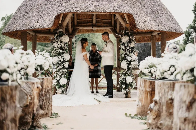Couple getting married beneath a thatched gazebo decorated by Emily&Me