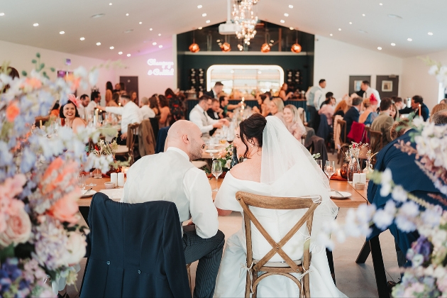 Bride and groom captured from behind as they look out over their guests seated at their wedding breakfast at Chapel House Estate