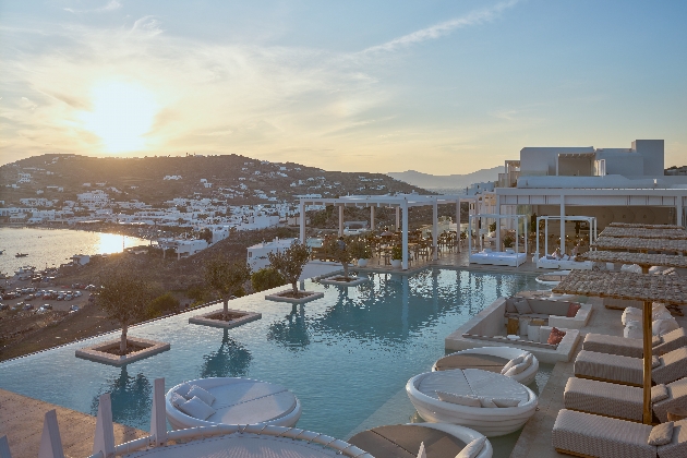 A rooftop swimming pool surrounded by sun loungers as the sun sets in the distance