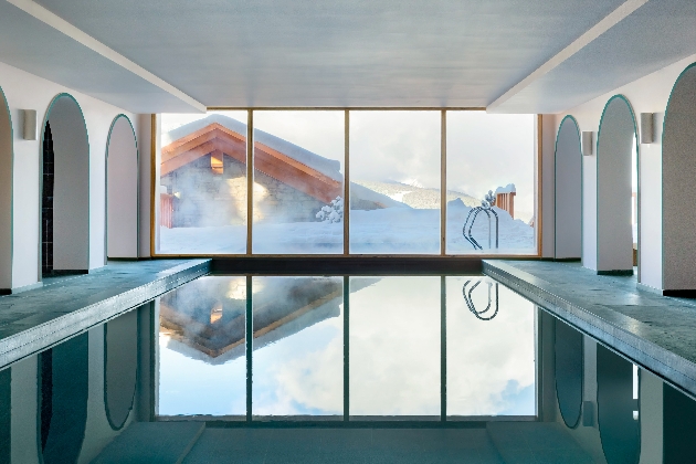 An indoor swimming pool in front of four large glass windows that show snow outside