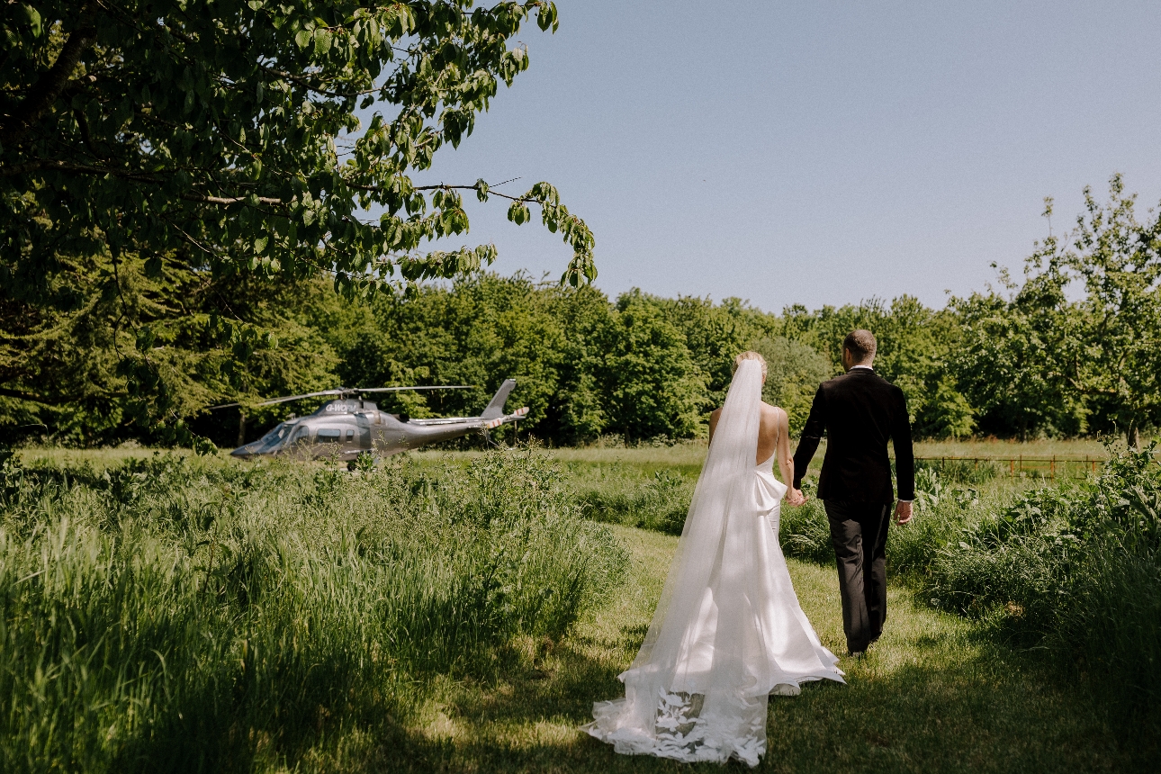 bride and groom walking through fields to helicopter
