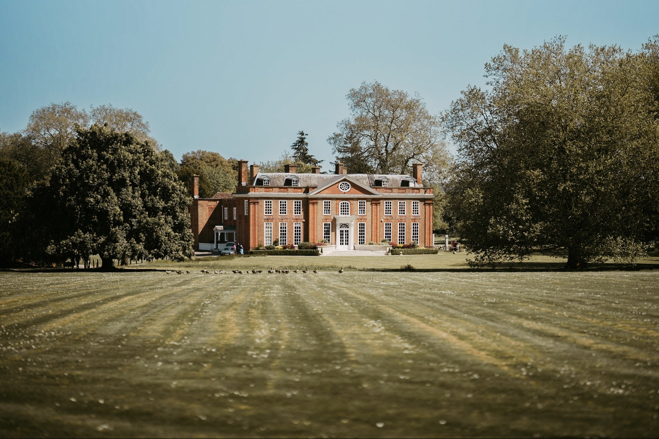 historic manor house at the end of a long grassed lawn with big trees 