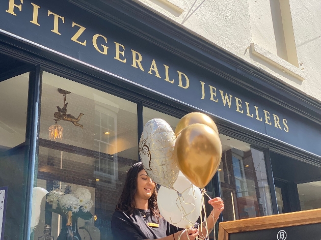 A woman holding balloons in front of a store with a sign that reads Fitzgerald Jewellers
