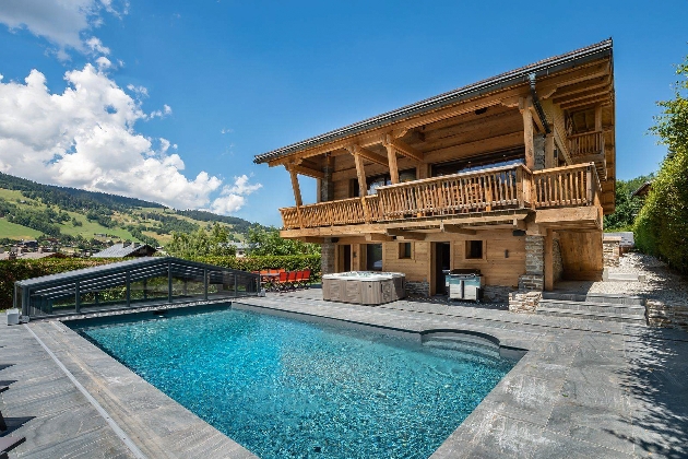 An outdoor swimming pool with a large wooden building next to it and views of the mountains