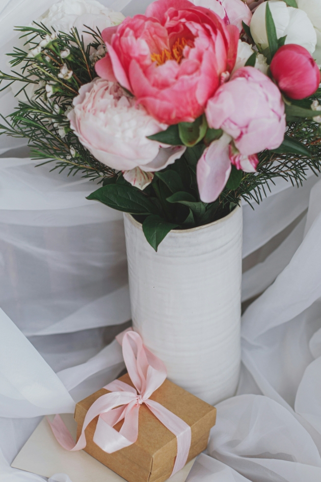 brown paper present with pink bow next to peonies in a vase
