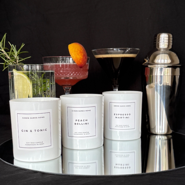 three candles and cocktails sat on mirror with cocktail shaker to the right