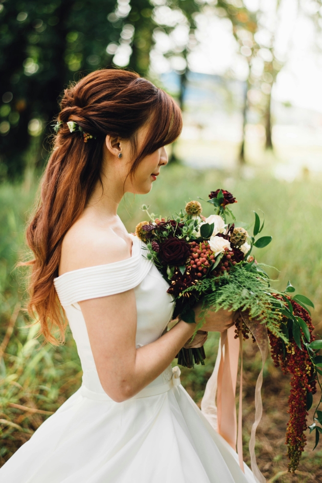 Woman in wedding dress posing with flowers in woodland area