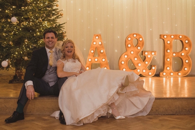 A bride and groom laughing in front of a Christmas tree and light-up letters