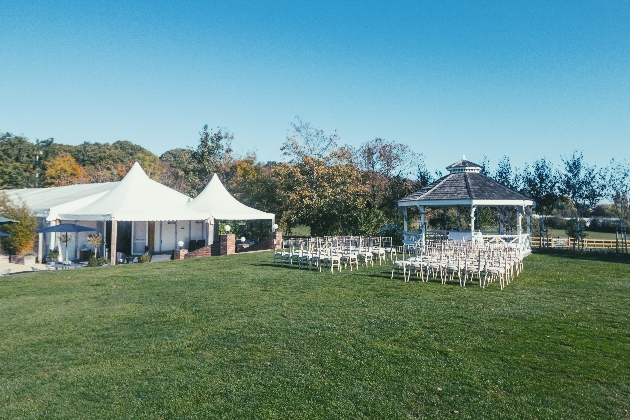 A gazebo with rows of white chairs in front of it and a marquee in the background