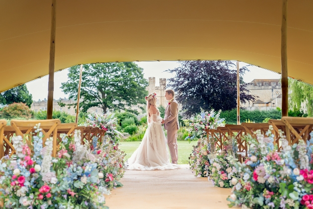 A bride and groom holding hands under a tent surrounded by flowers
