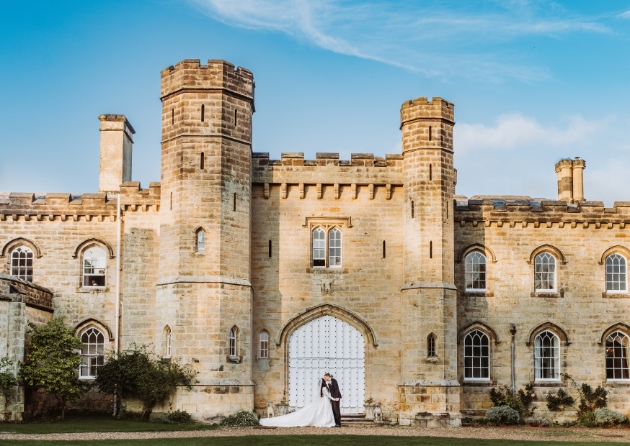 The exterior of a castle with a bride and groom kissing in front of it