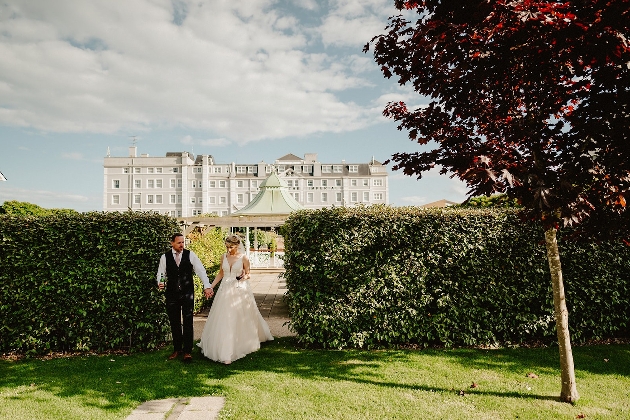 A bride and groom walking with a grand building in the background